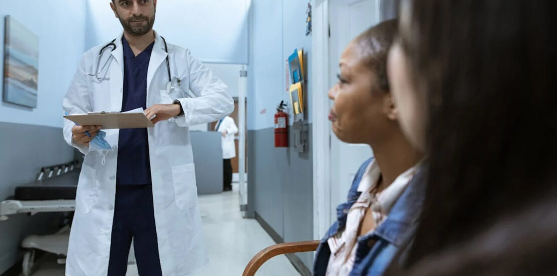 Doctor discussing patient billing with two women in a clinic hallway for medical claim denial management. | medical claim denial management