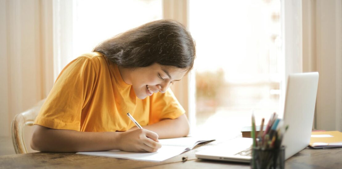 Woman at desk with pen and paper using laptop studying for medical billing certification requirements. | medical billing certification requirements