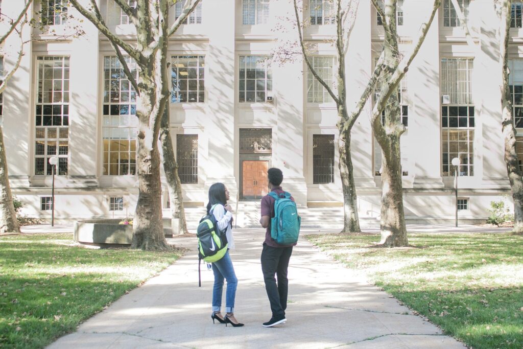 Two students with backpacks outside a college building, representing medical billing education requirements. | medical billing educational requirements