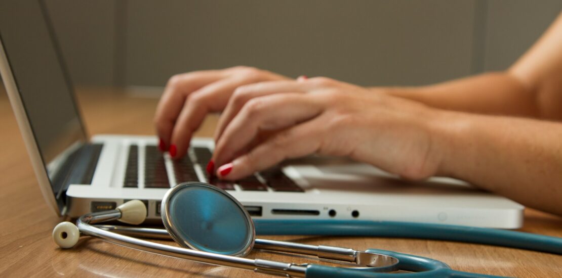 Hands typing on a laptop with a stethoscope, representing types of medical billing in healthcare. | types of medical billing